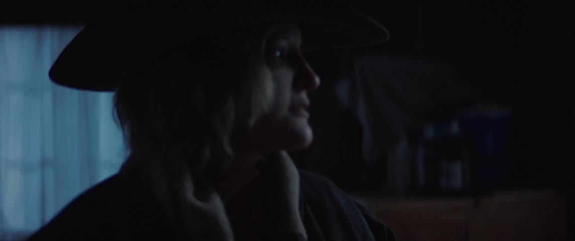 A person putting on a jacket while wearing a cowboy hat in a dark room