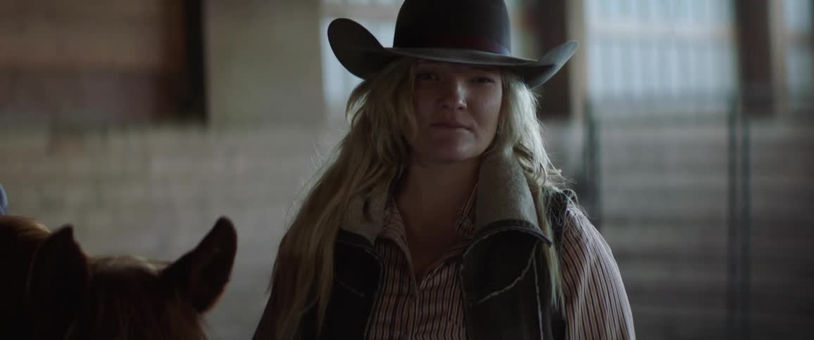 Cowgirl standing next to a horse inside a stable