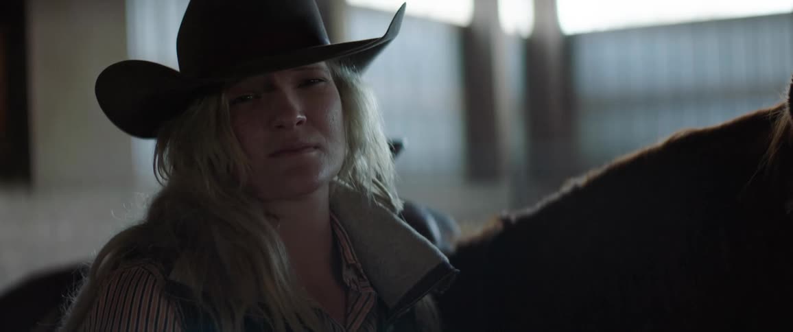 Cowgirl wearing a cowboy hat next to a horse inside a stable