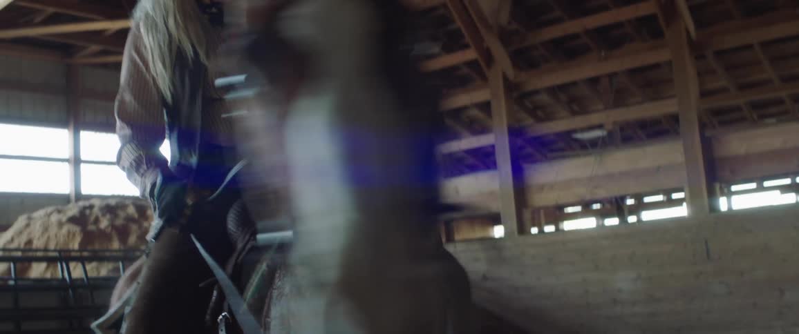 A woman with a hat and gloves riding a horse with a wall and windows in the background