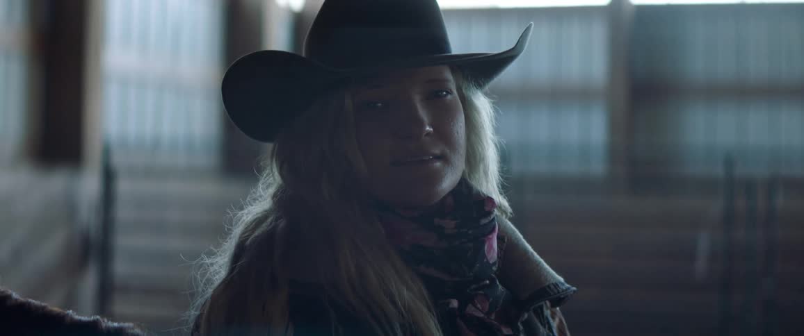 A cowgirl is sitting in the dark barn