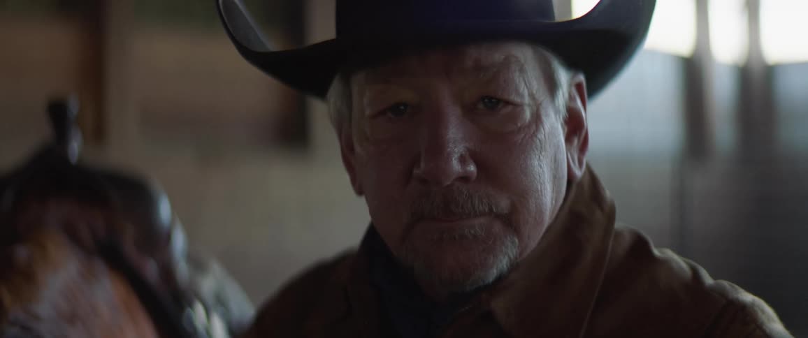 A rancher in a cowboy hat poses with a hand on his horse