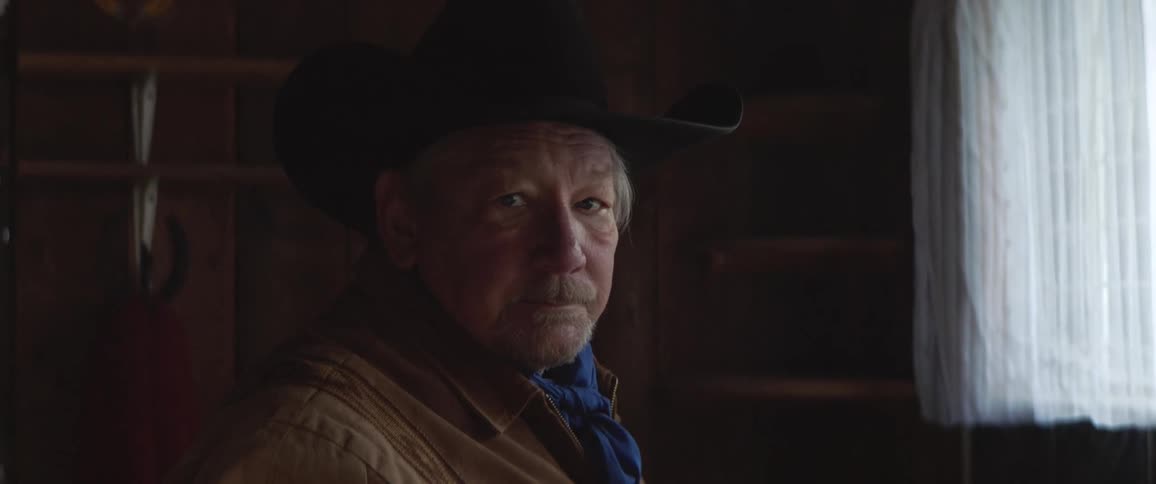 A rancher poses in his cowboy hat while standing indoors next to a window