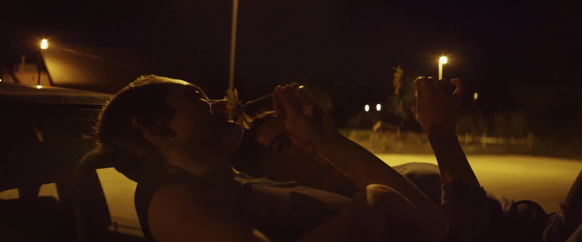 Young couple resting over the windshield of a parked car smelling flowers together at night