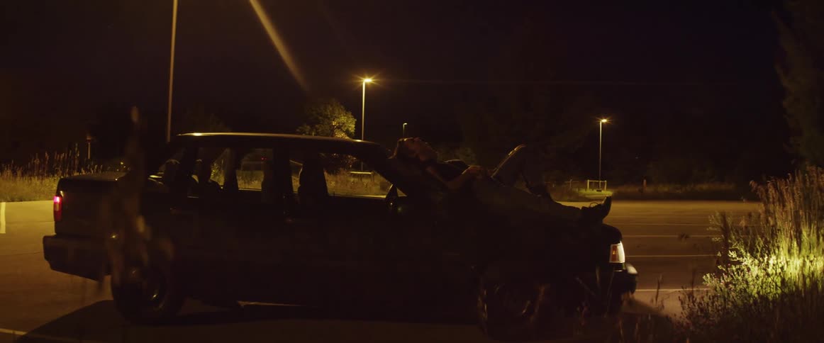 A couple lying on the hood of a car point up to the sky as they star gaze