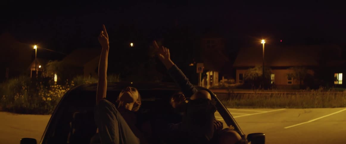 Two young people laying on hood of car pointing up at stars and talking