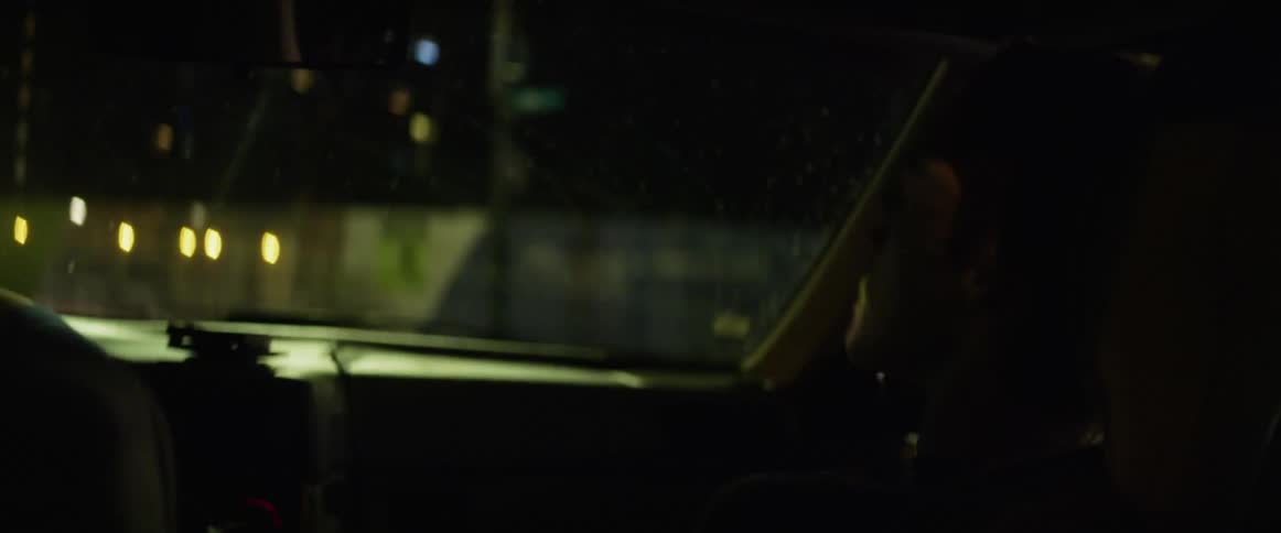A boy riding in a vehicle with a windshield with vehicles the streets and the sky in the background
