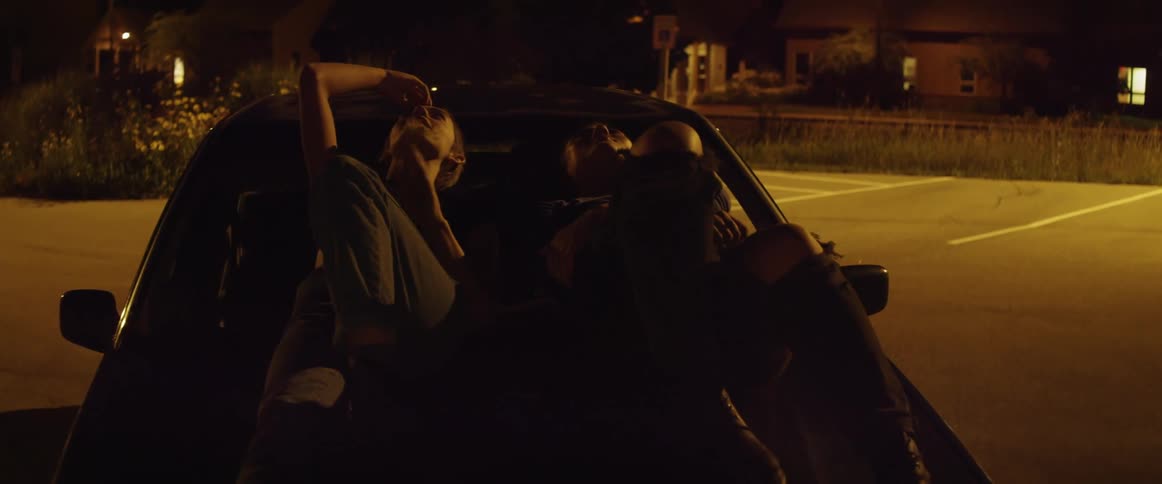 Two friends talk while lying on the hood of their car and looking up at the sky