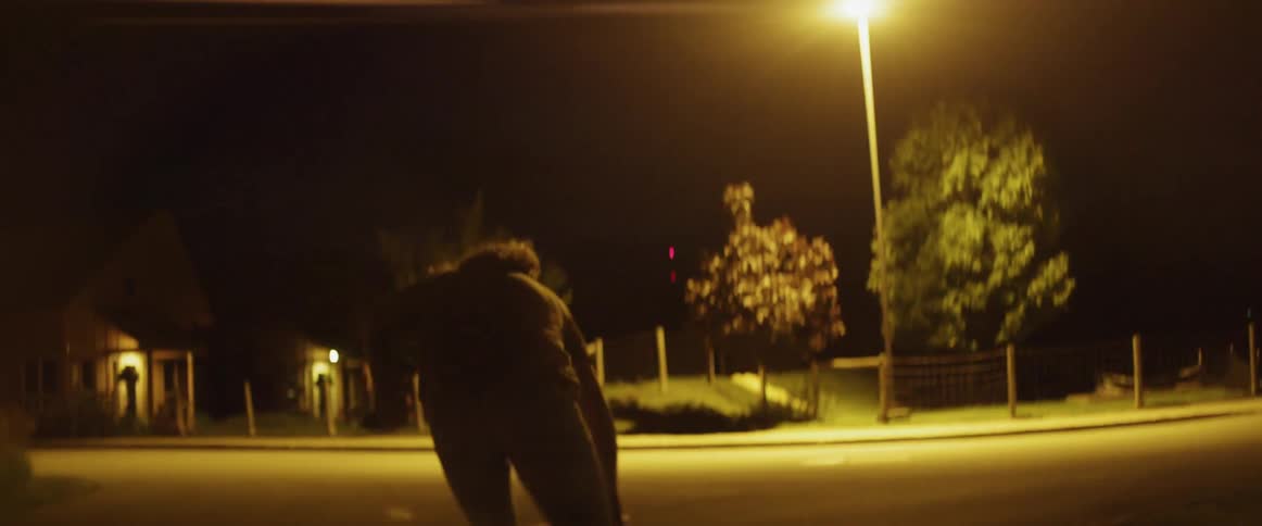 A man riding a skateboard in a parking lot with houses trees and the sky in the background