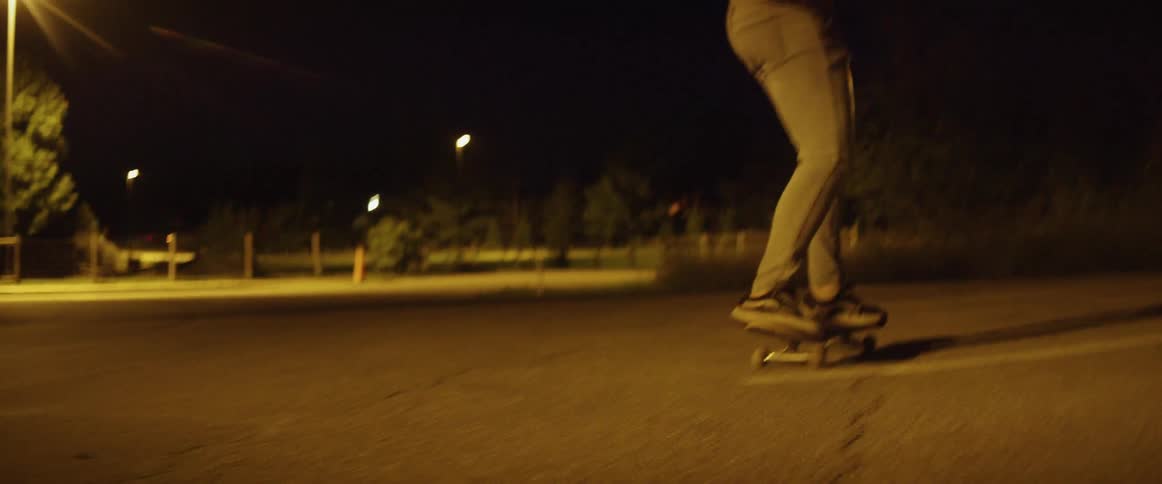 A man skating on a skateboard in a parking lot with trees streetlights and the sky in the background