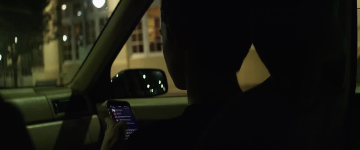 Woman sitting in a car driving on the city at night texting on her phone