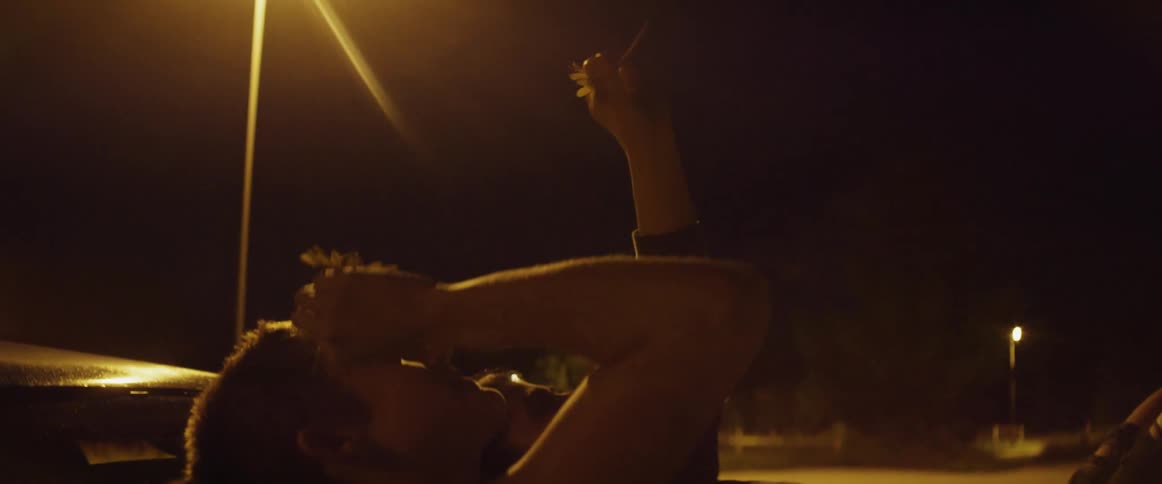 Young couple resting over the windshield of a parked car smelling flowers together at night