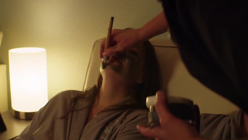 A salon employee paints a facial mask on a woman