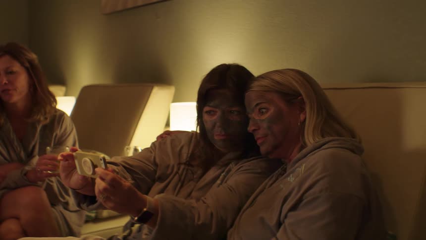 Two women laughing and taking a selfie while wearing mud masks at a spa