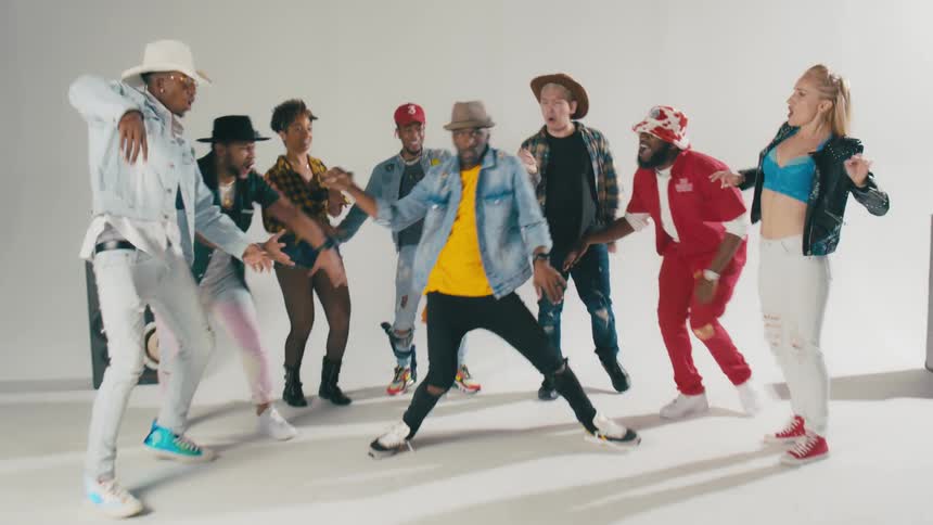 A group of people cheer on a man as he dances in a white studio