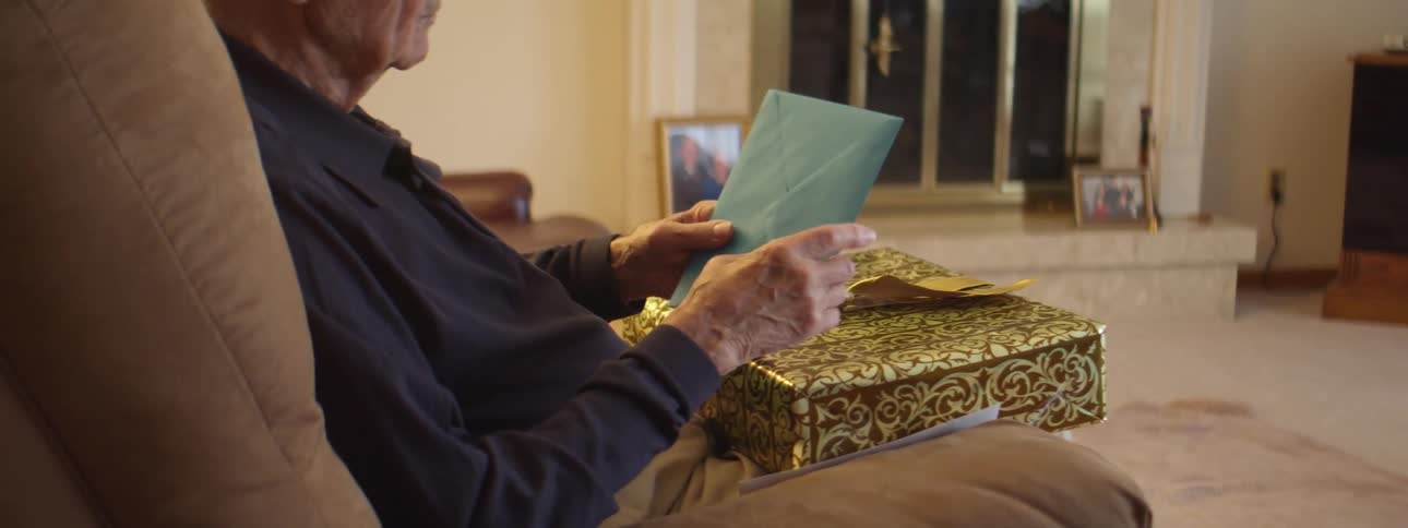 Elderly man sitting in a couch in the living room opens a gift