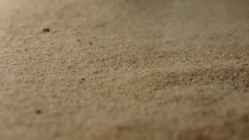 Sand particles moving across the top of sand on the ground