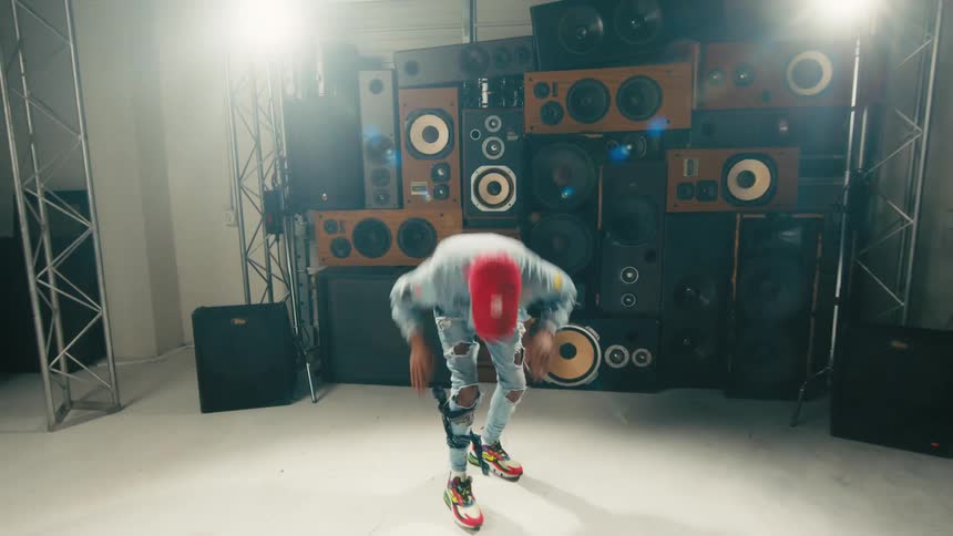 A man smiling and dancing in front of a stack of large speakers