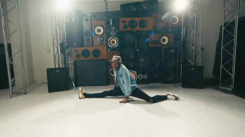 A man in a denim jacket dancing in front of a pile of speakers indoors