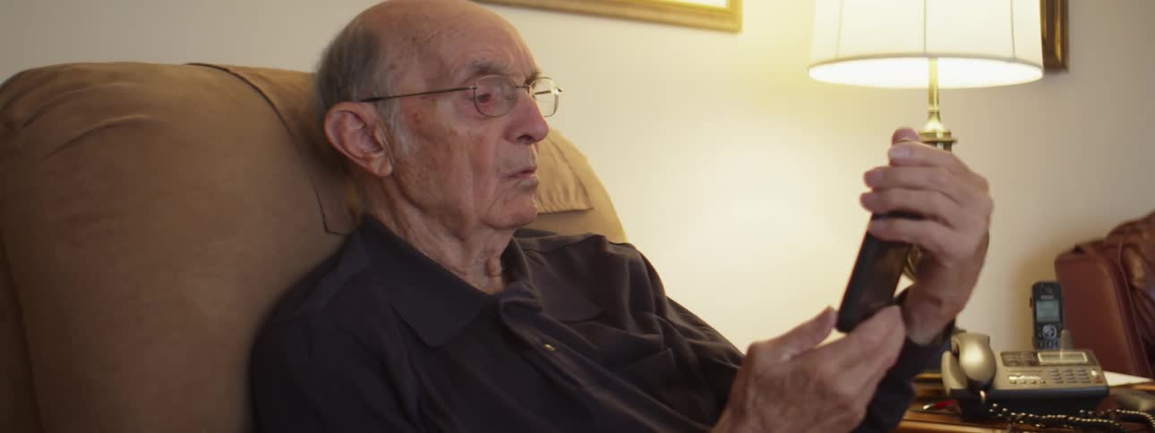 Senior citizen sitting in a couch at home checks his phone