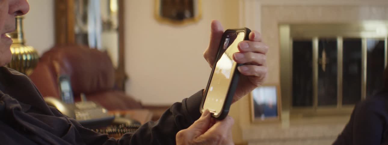 A man sits in an armchair and holds his phone out during a video call