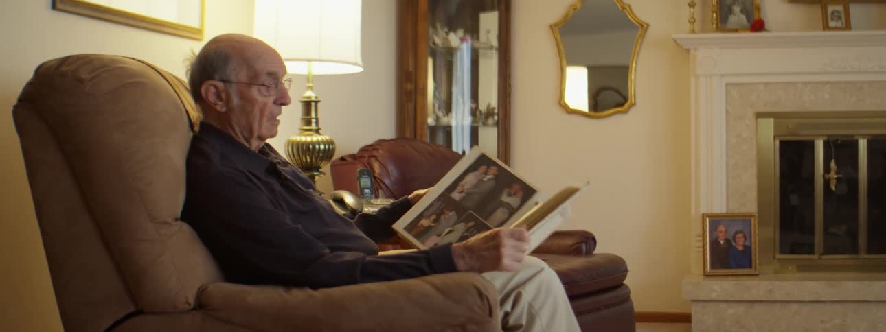 An elderly man flipping through a photo album while sitting in a living room chair