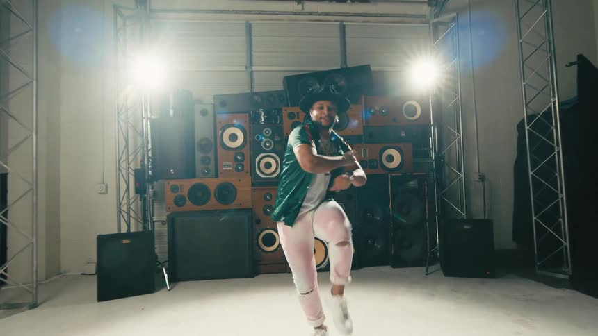 A man performs a hip hop dance in front of a large array of stereo speakers