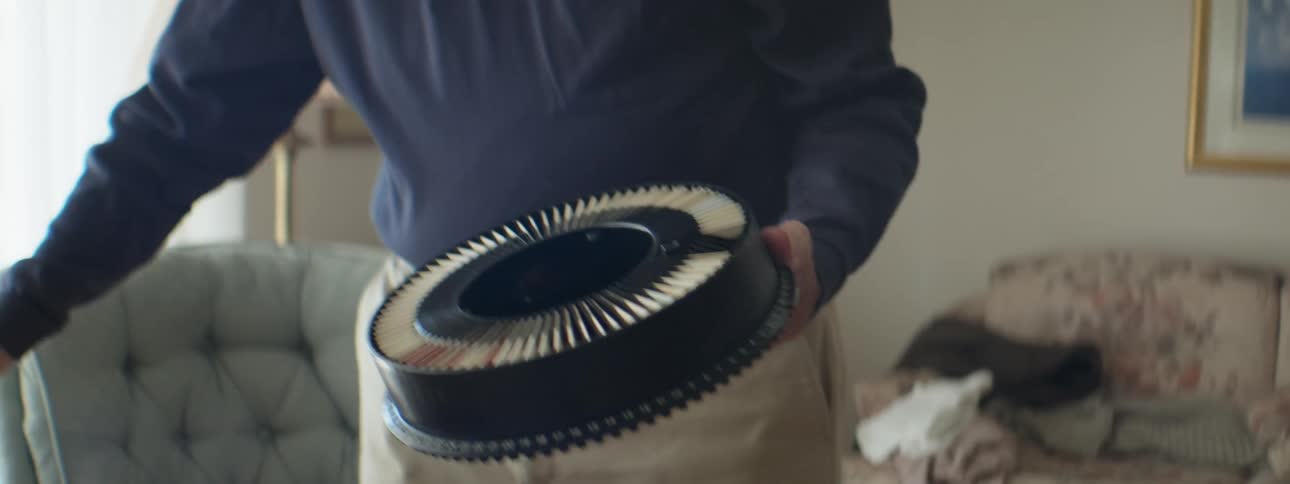 An elderly man holding a round container while standing in a living room