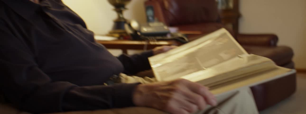 Elderly man sitting in the living room looking at photographs in an album
