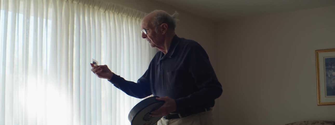An elderly man standing in a living room holding something in his hand