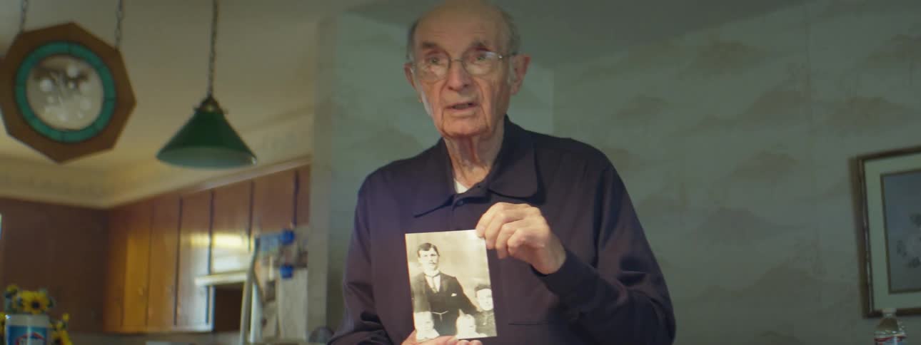 An elderly man talking about a vintage photograph he is holding