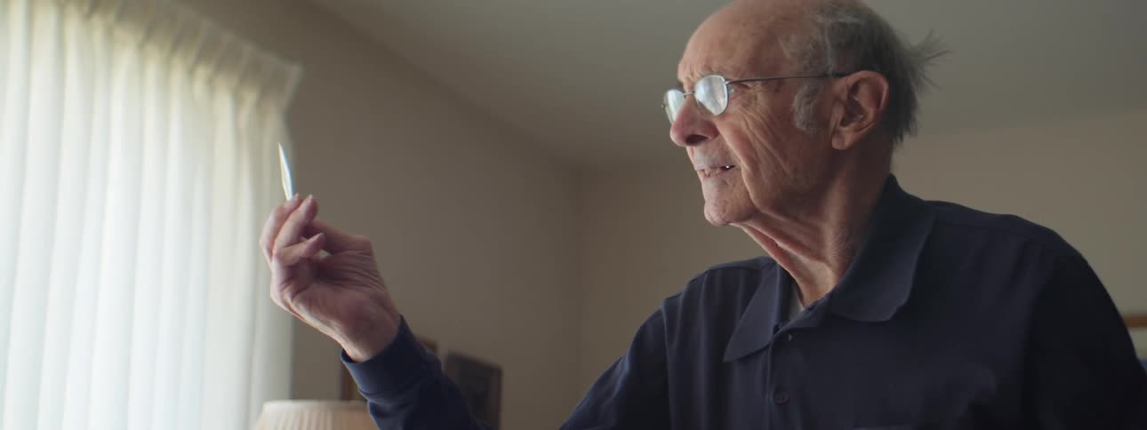 A man with glasses in a room with a lamp a wall and window in the background