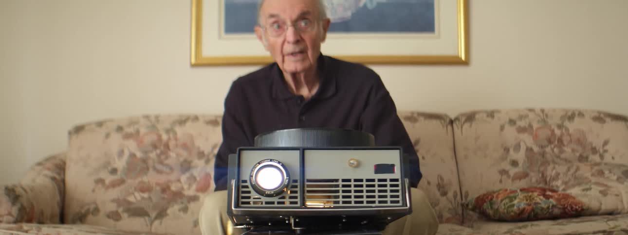 A man in a room sitting on a couch with a projector on books on a table