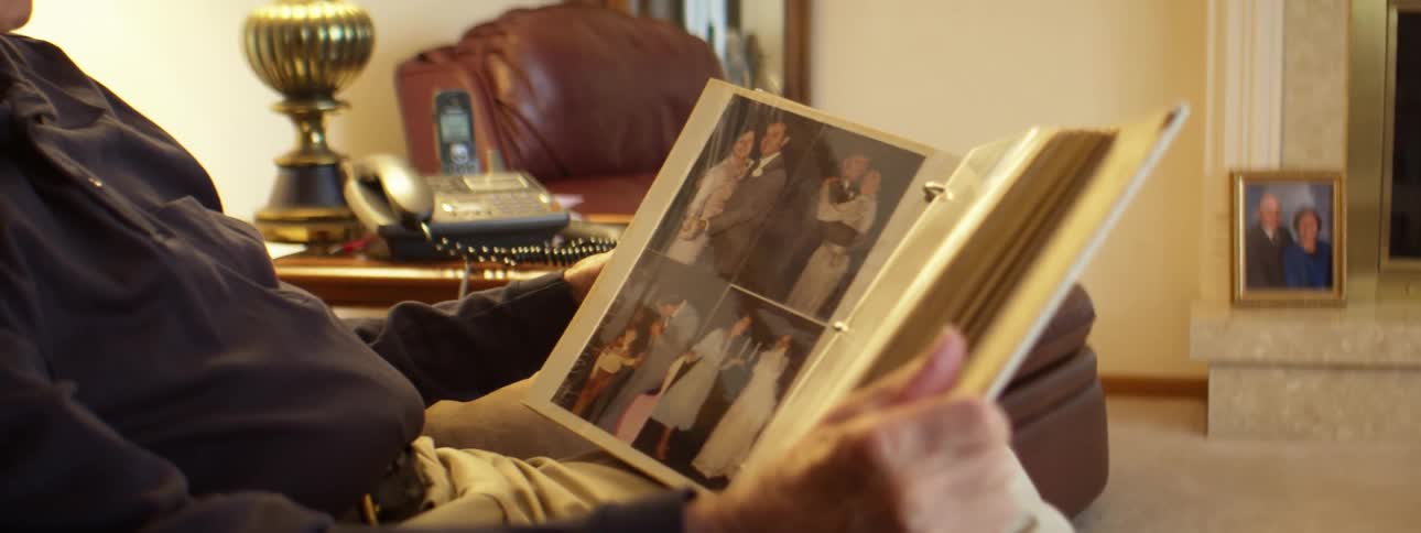 Elderly man sitting in the living room looking at photographs in an album