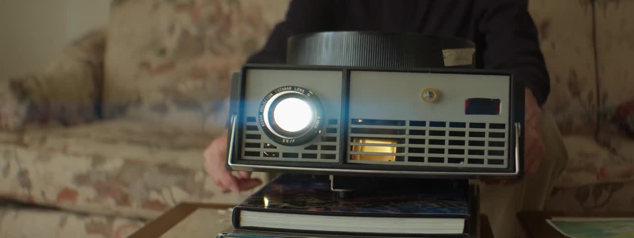 A person in a room sitting on a couch with a projector on books on a table