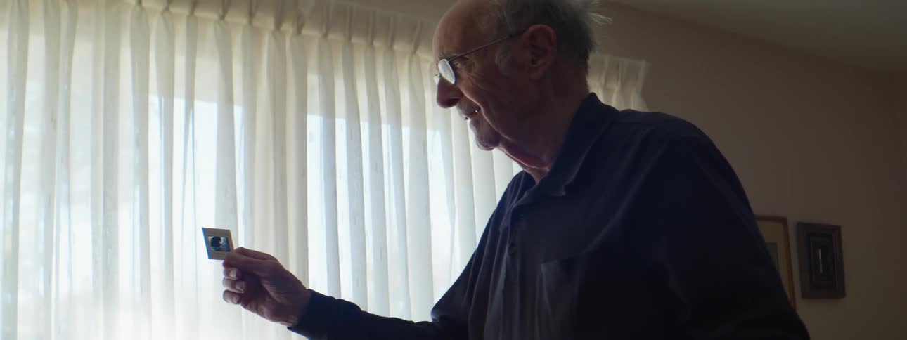 Elderly man standing in a room holds a slide on his hand