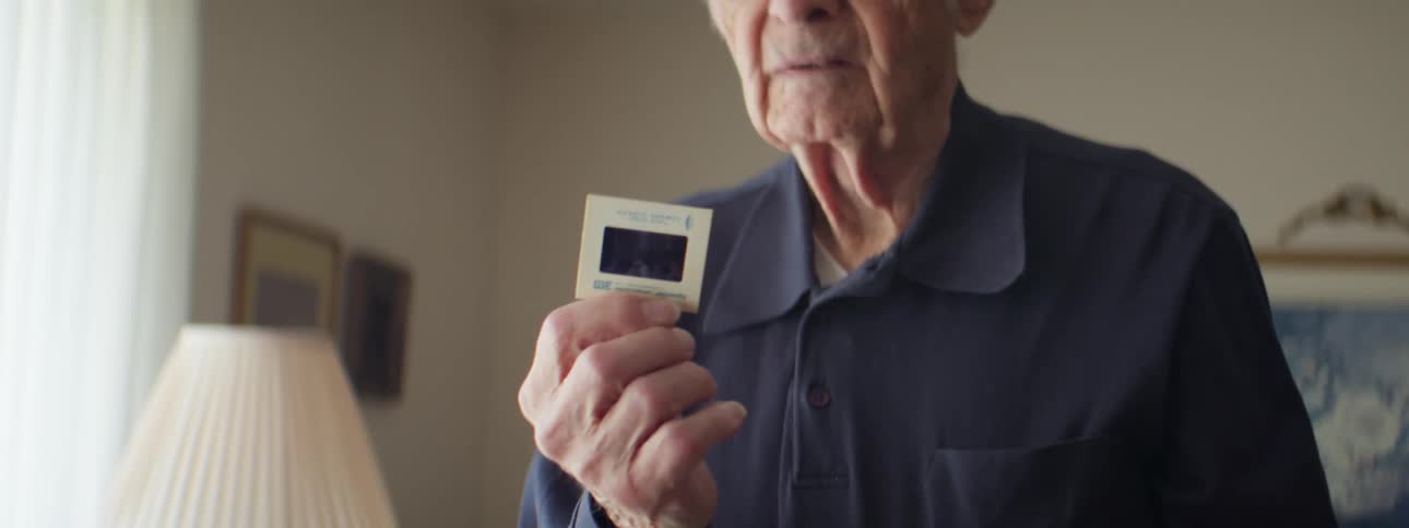 An elderly man removing a photo negative from a box while standing in a living room