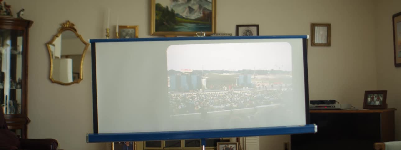 Old school photos flash across a roll down projector screen inside of a living room