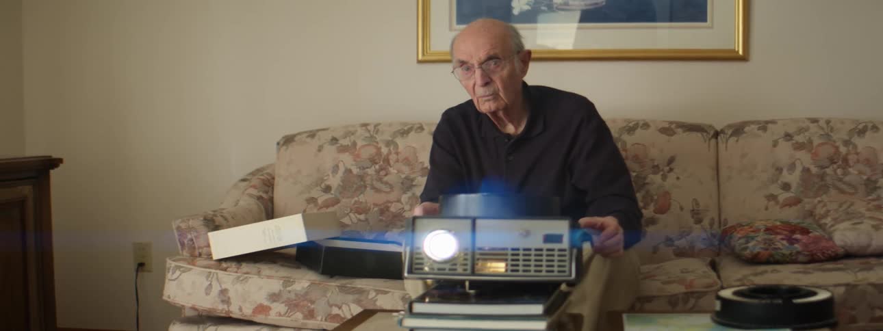 Elderly man sitting on couch runs slide projector