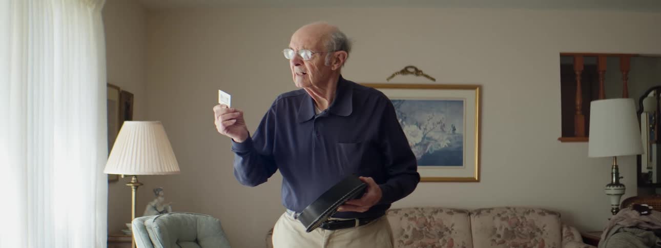 Elderly man standing inliving room views slides before setting them into slide projector