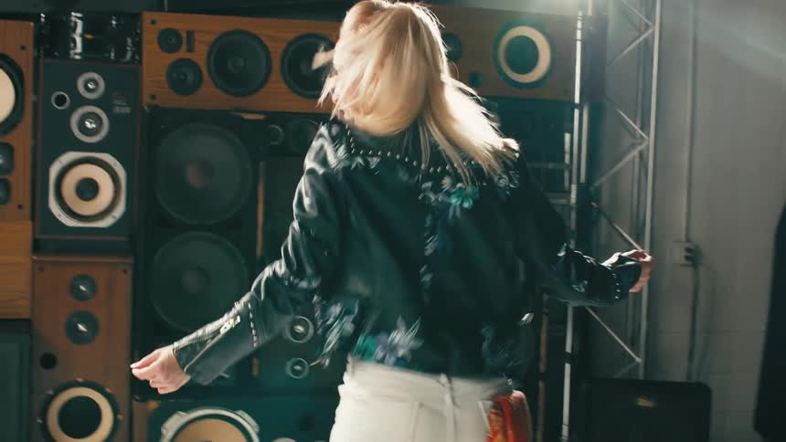A woman with a jacket dancing with speakers and lights in the background