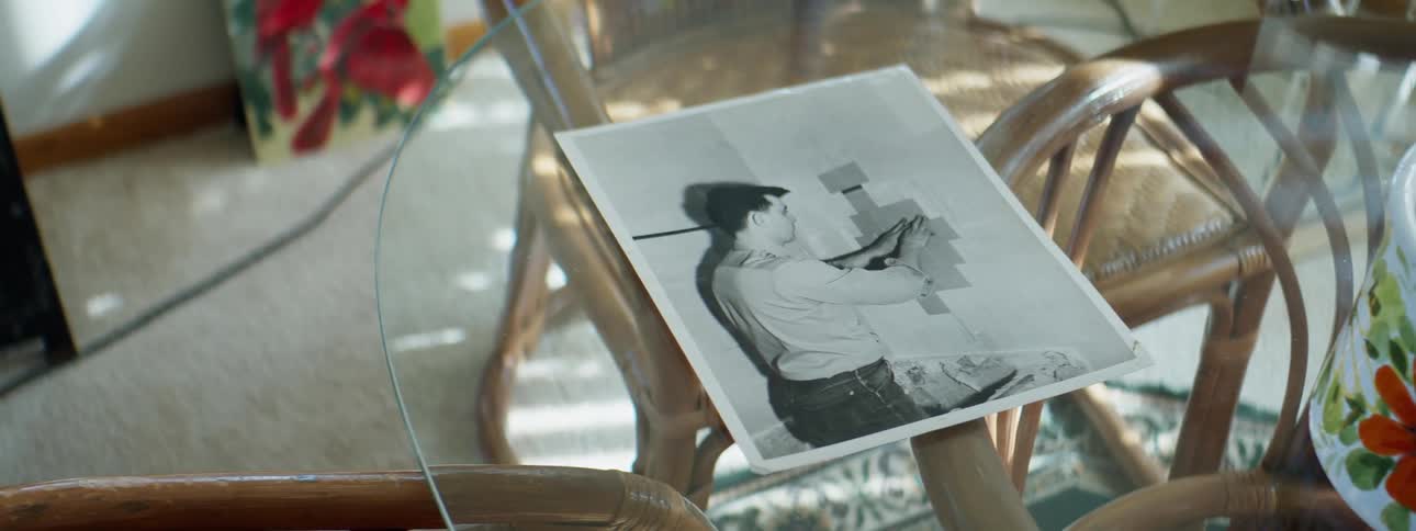 A photograph in a room with a glass table and chairs with a wall in the background