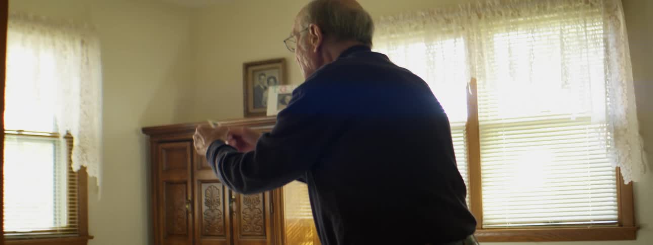 A man lifts a slide out of a projector wheel in a box on a bed and holds it up to the light