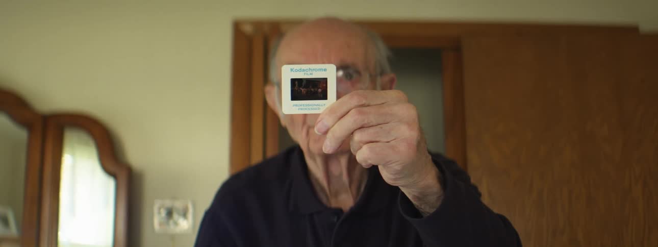 Elderly man standing in a room at home holding a slide on his hand