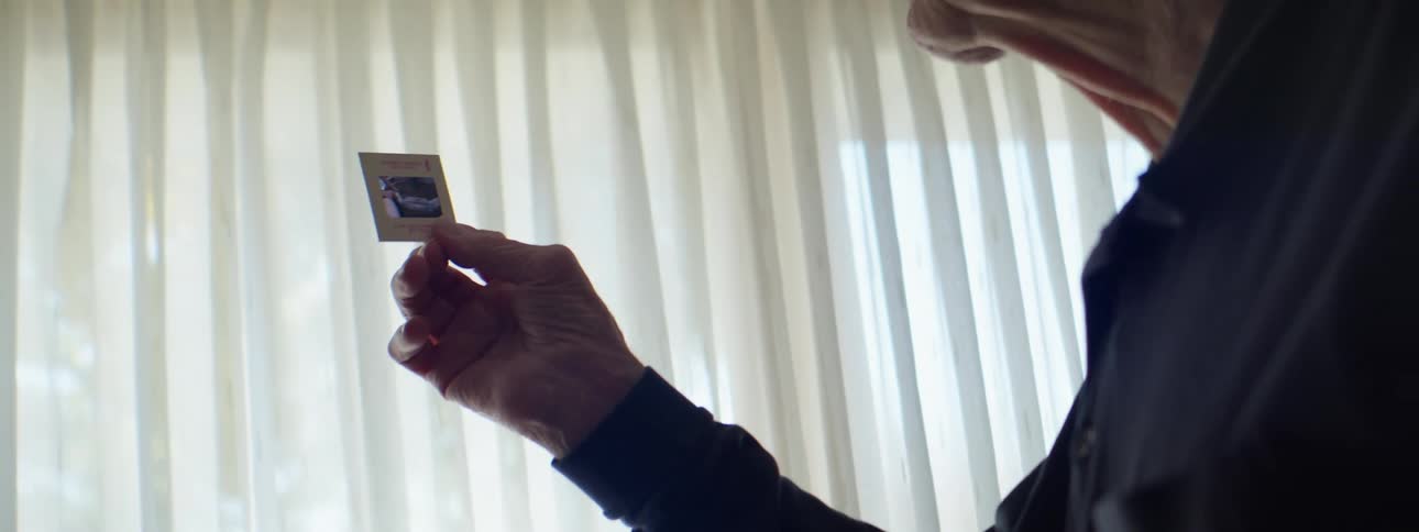 Elderly man inspecting vintage film slide in front of window