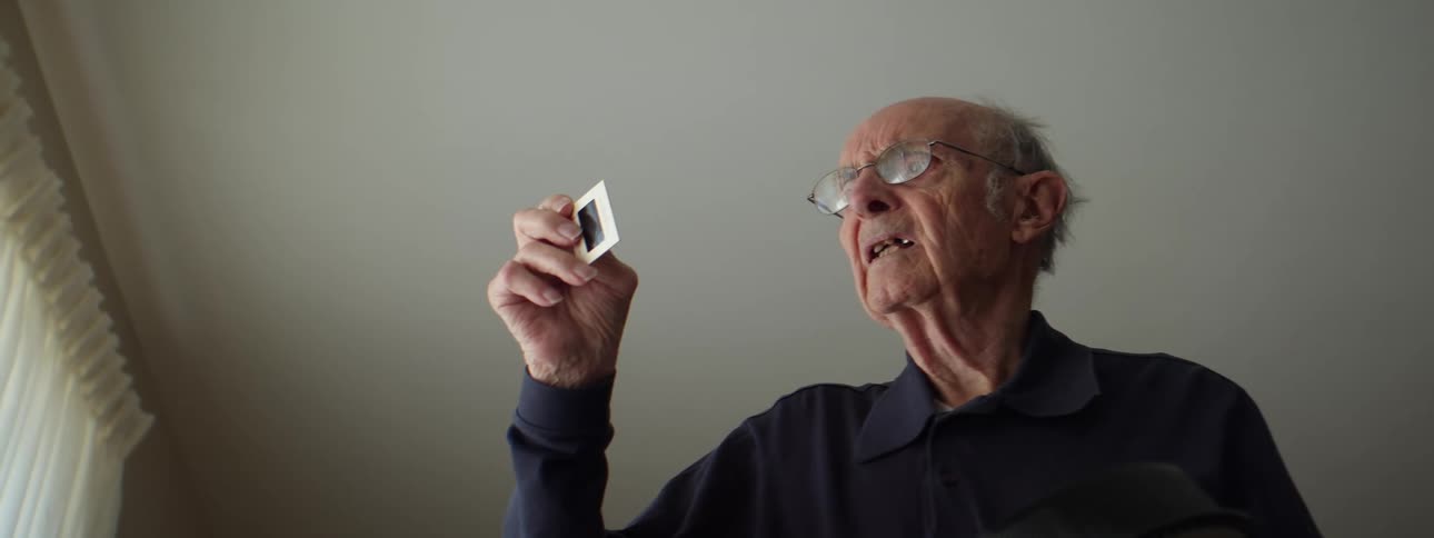 A man with glasses in a room with a wall and window in the background