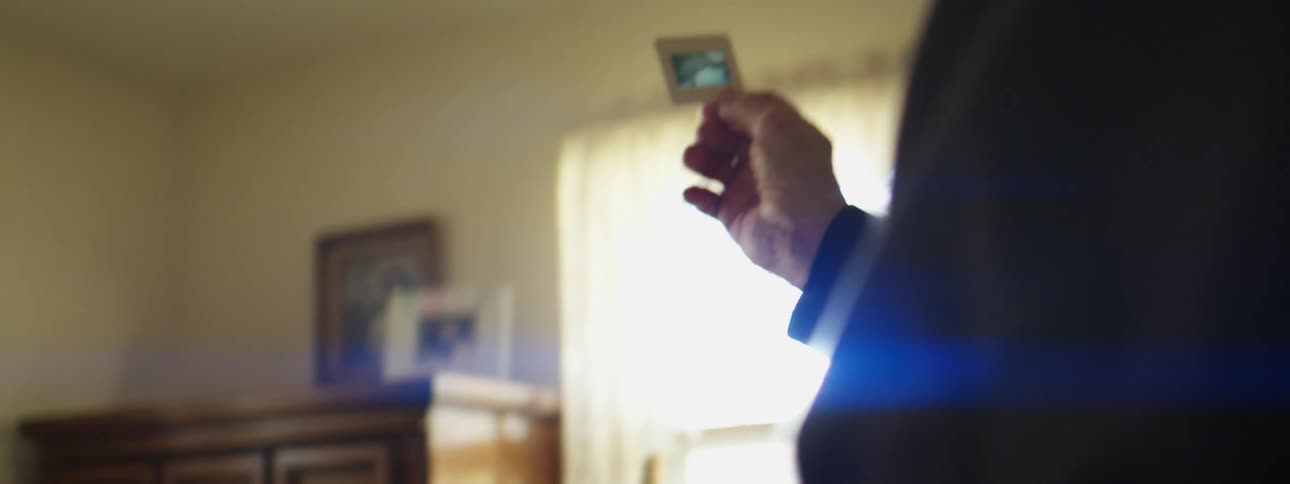 An elderly man is in a bedroom viewing picture slides