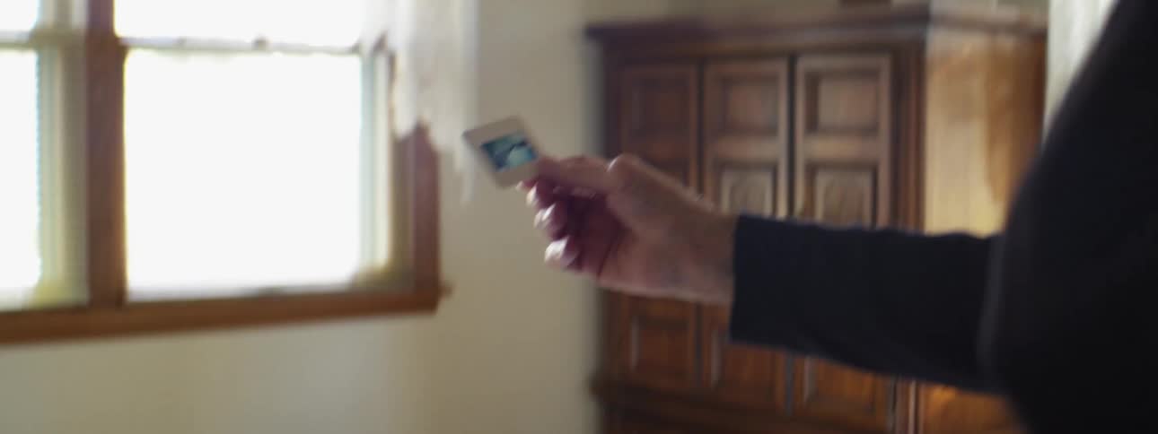 An elderly man is in a bedroom looking at picture slides near a bed
