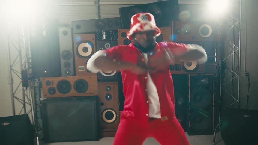 Man dressed in colorful red clothes energetically dancing in front of a tower of speakers