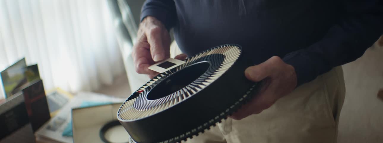 A person in a room holding projector slides with a window and blinds in the background